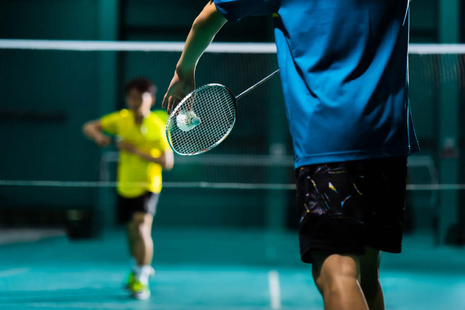 Spieler*in schlägt fokussiert einen Federball im Badmintonspiel.