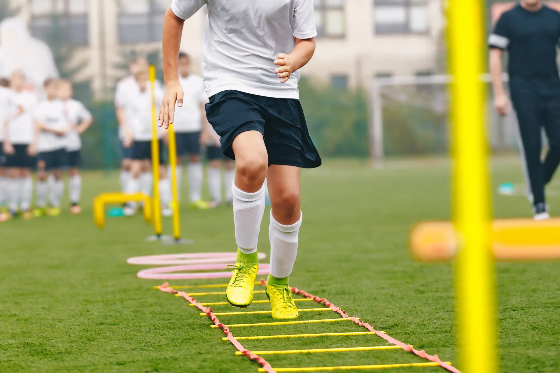 Junge Fußballspieler*innen trainieren mit Koordinationsleiter auf dem Rasen.